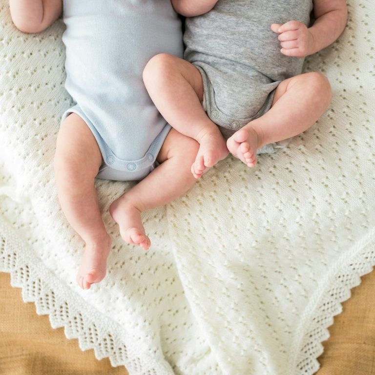 Zwei Babys liegen nah nebeneinander auf einer Decke